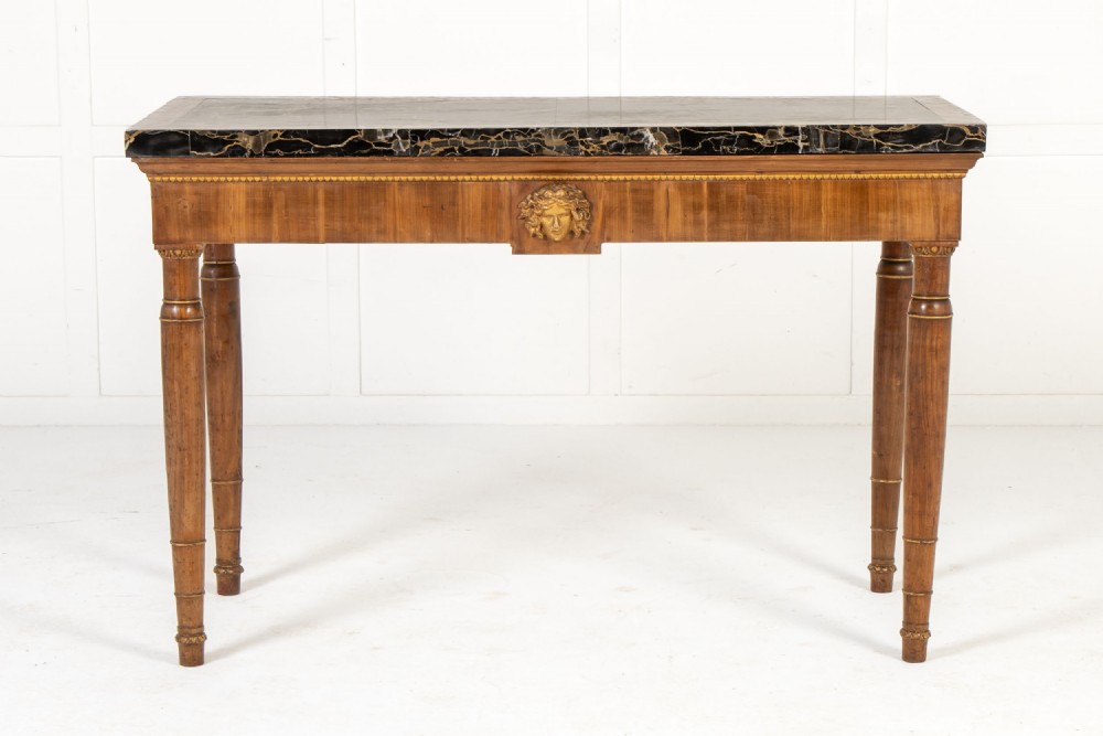 A 19th-century Italian walnut console table with a black marble top, gilt mask motif, and tapered legs.