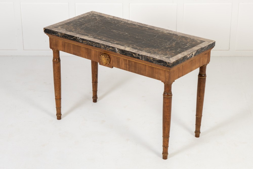 A 19th-century Italian walnut console table with a black marble top, gilt mask motif, and tapered legs. View V
