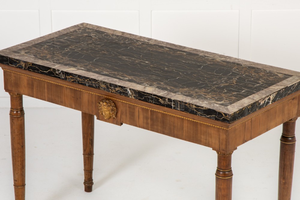 A 19th-century Italian walnut console table with a black marble top, gilt mask motif, and tapered legs. View VI