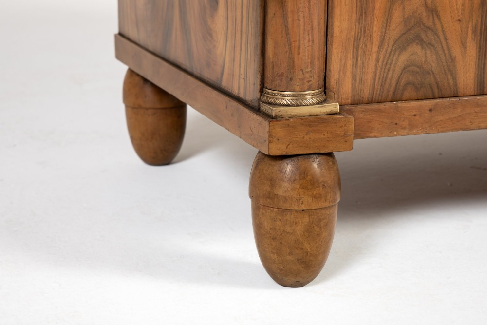 A 19th-century Italian walnut commode featuring a grey marble top, three drawer fronts with bookmatched grain, flanking column pilasters with brass mounts, and turned feet. View V