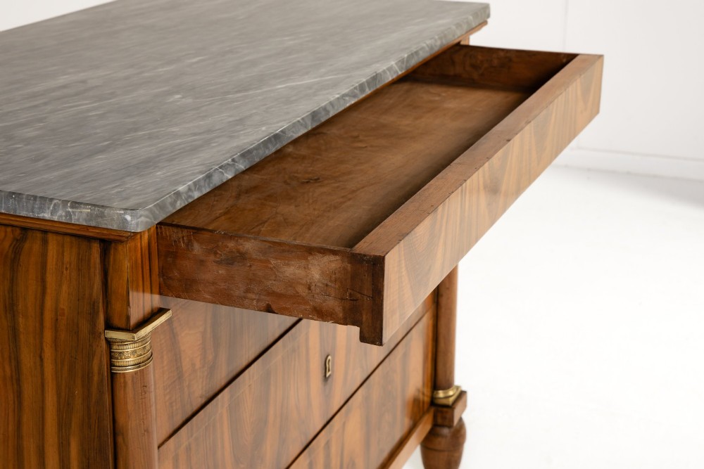 A 19th-century Italian walnut commode featuring a grey marble top, three drawer fronts with bookmatched grain, flanking column pilasters with brass mounts, and turned feet. View VI