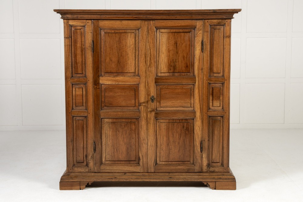 An 18th-century Italian walnut cabinet featuring twin raised geometric panel doors, moulded side panels, iron hardware, and a stepped plinth base.