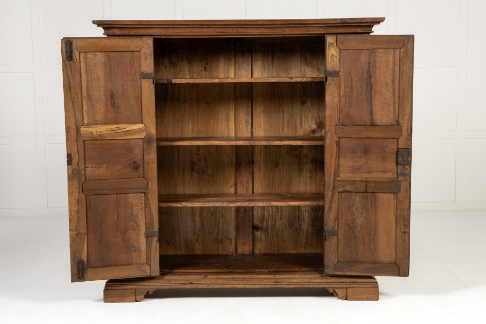 An 18th-century Italian walnut cabinet featuring twin raised geometric panel doors, moulded side panels, iron hardware, and a stepped plinth base. View V