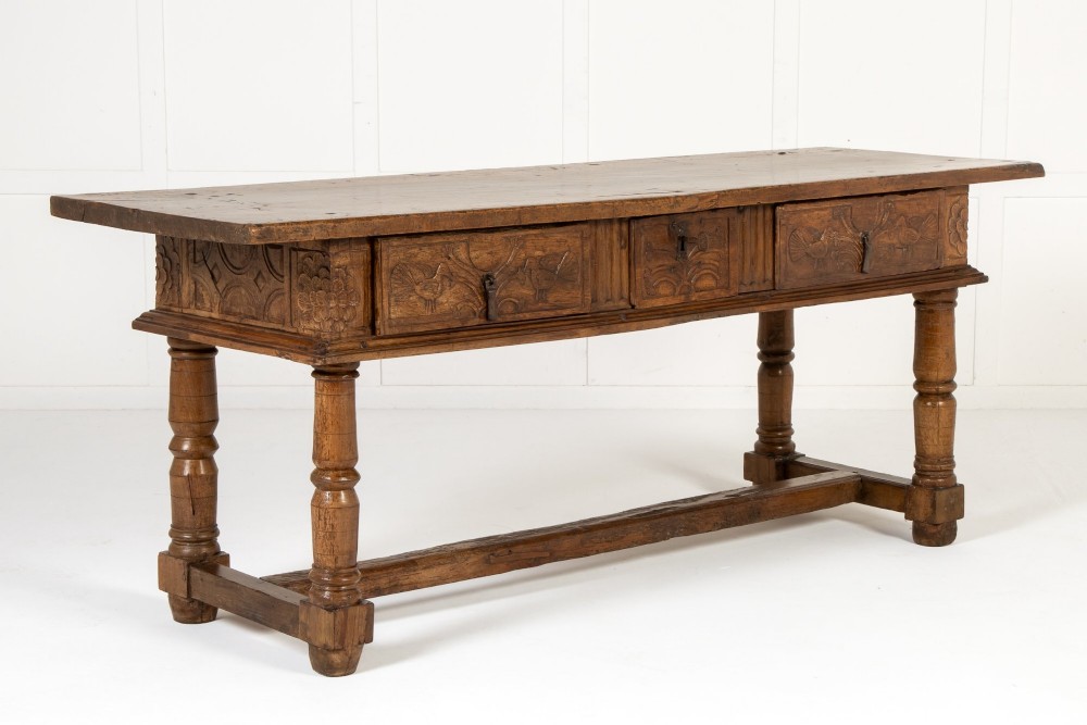 A 17th-century Spanish walnut side table featuring three carved drawer fronts, turned legs, and a low stretcher base.