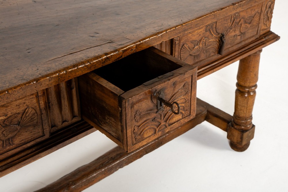 A 17th-century Spanish walnut side table featuring three carved drawer fronts, turned legs, and a low stretcher base. View VI