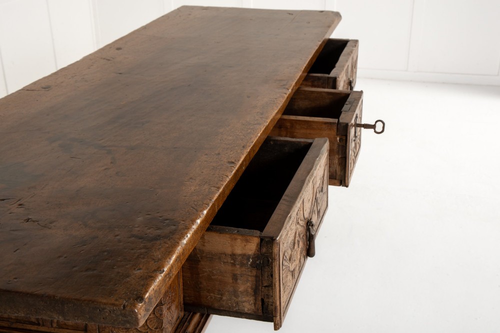 A 17th-century Spanish walnut side table featuring three carved drawer fronts, turned legs, and a low stretcher base. View X