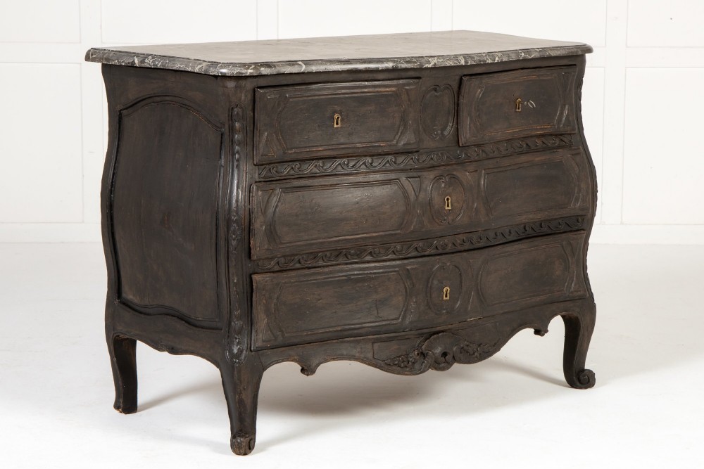 An 18th-century ebonised French bombe commode featuring three drawers, carved panels, a grey marble top, and brass keyholes. View II