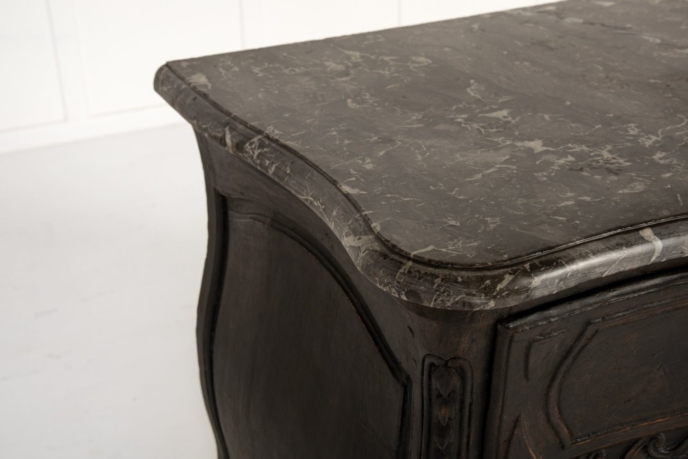 An 18th-century ebonised French bombe commode featuring three drawers, carved panels, a grey marble top, and brass keyholes. View III