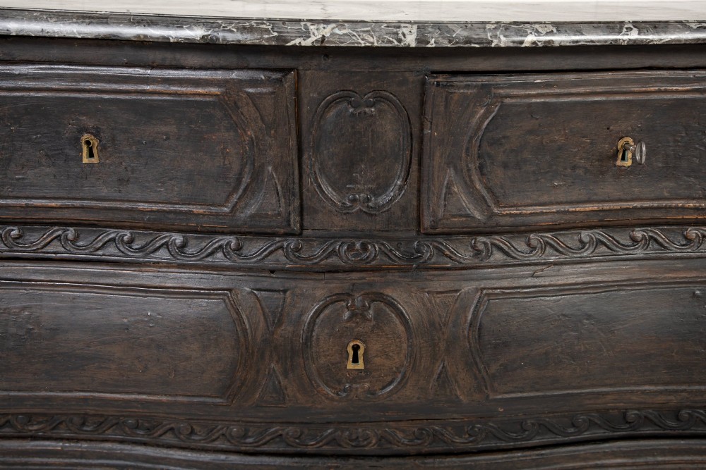 An 18th-century ebonised French bombe commode featuring three drawers, carved panels, a grey marble top, and brass keyholes. View V