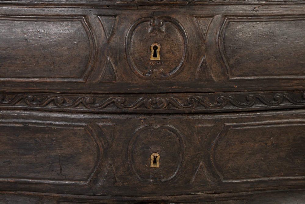 An 18th-century ebonised French bombe commode featuring three drawers, carved panels, a grey marble top, and brass keyholes. View VII