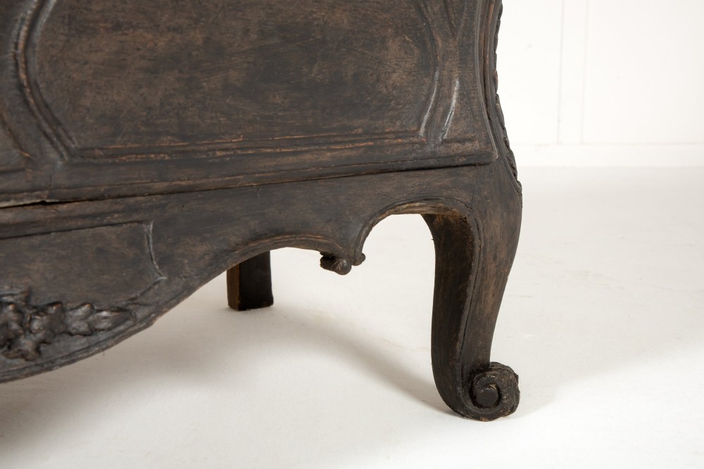 An 18th-century ebonised French bombe commode featuring three drawers, carved panels, a grey marble top, and brass keyholes. View XI