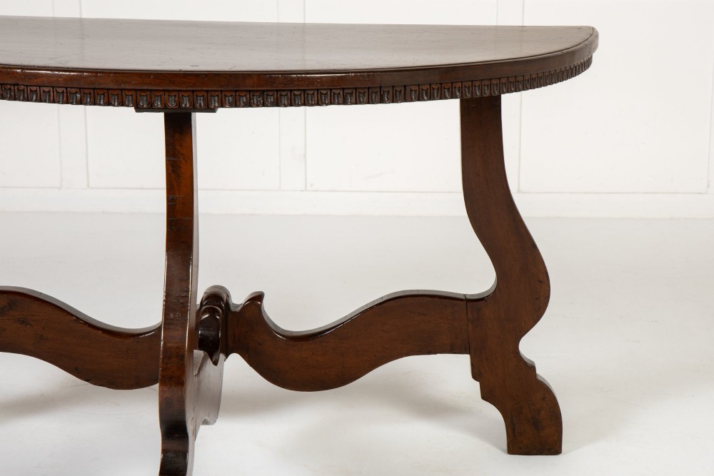 A pair of 18th-century Italian walnut demi-lune console tables with carved dentil edges, shaped legs, and central stretchers. View IV