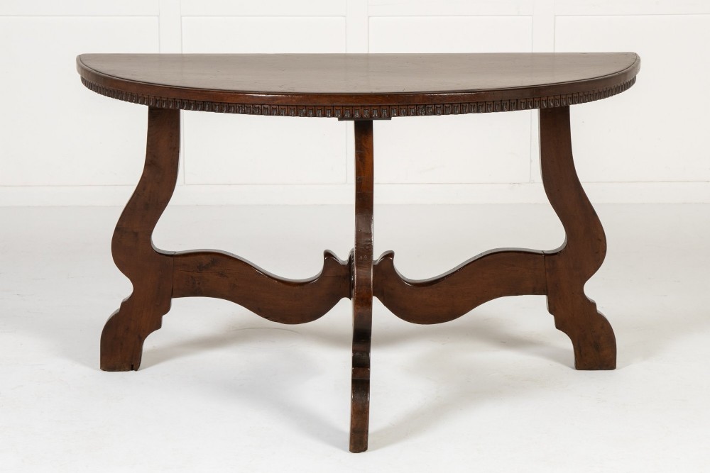 A pair of 18th-century Italian walnut demi-lune console tables with carved dentil edges, shaped legs, and central stretchers. View V
