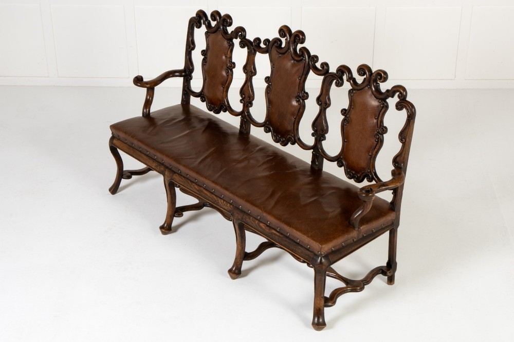A 19th-century carved walnut settee featuring a triple chair-back design with scrollwork carving and a brown leather studded seat. View III