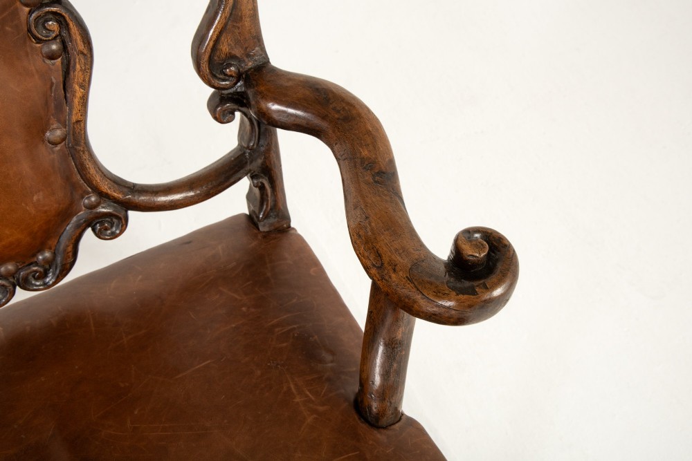A 19th-century carved walnut settee featuring a triple chair-back design with scrollwork carving and a brown leather studded seat. View VII