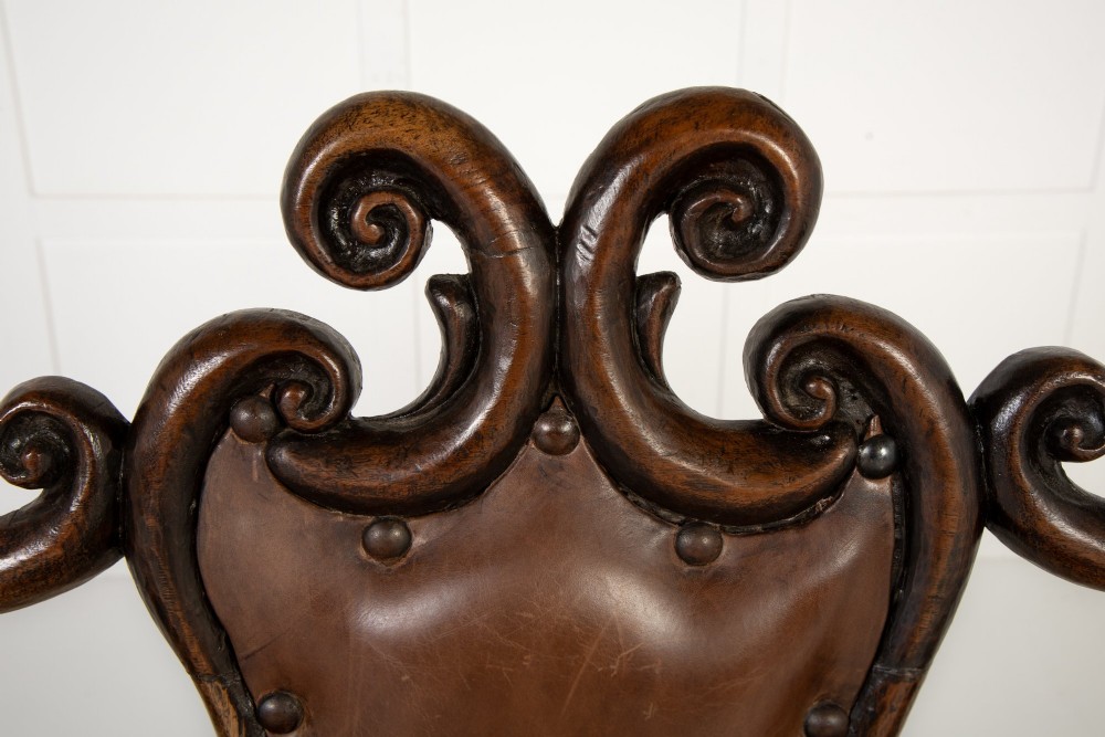 A 19th-century carved walnut settee featuring a triple chair-back design with scrollwork carving and a brown leather studded seat. View VIII