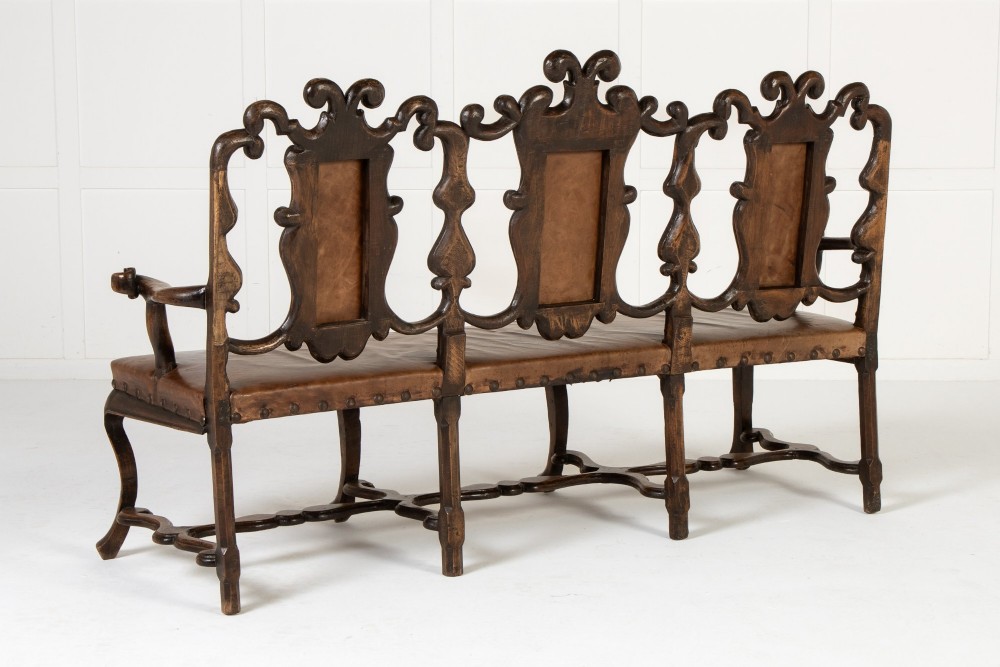 A 19th-century carved walnut settee featuring a triple chair-back design with scrollwork carving and a brown leather studded seat. View X