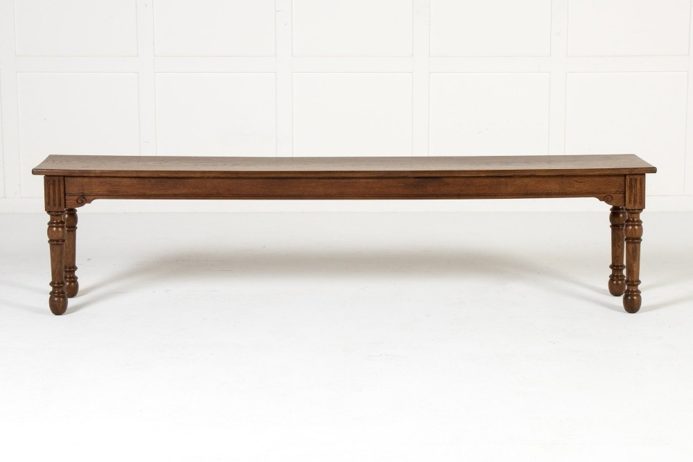 A long 19th-century dark oak bench featuring a rectangular plank seat supported by turned legs with fluted frieze details. View II