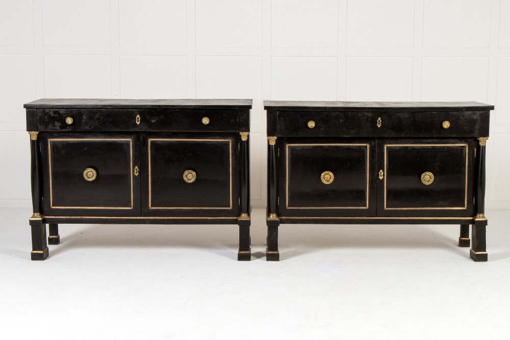A pair of matching 18th-century Italian ebonised side cabinets featuring gilt metal mounts, fluted corner columns, single top drawers, and double panelled doors.