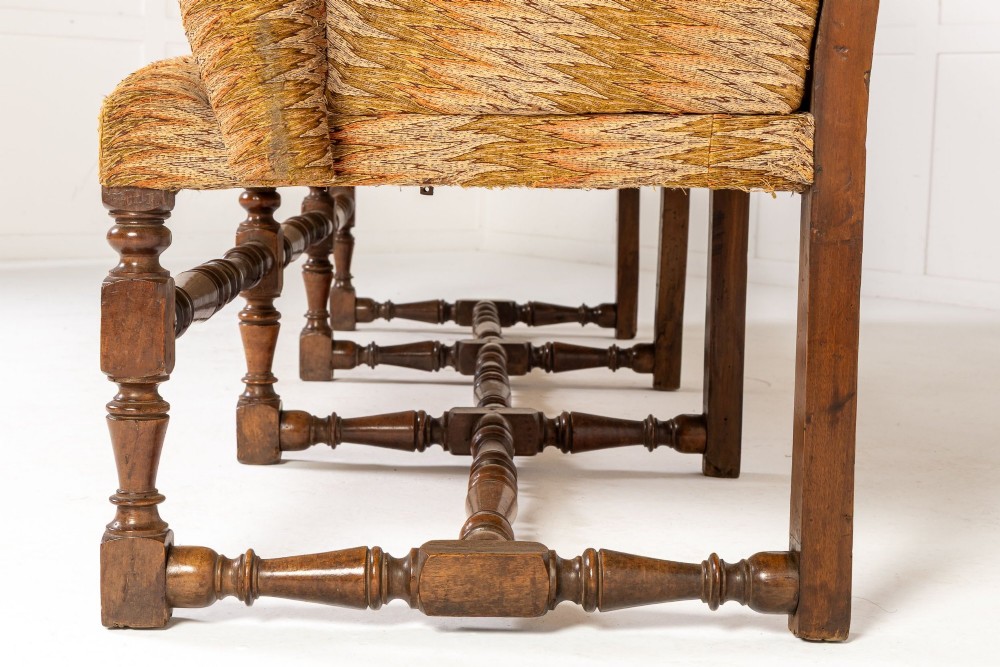 An 18th-century Italian walnut settee featuring high-backed wings, flame-stitch patterned upholstery in warm ochre tones, and six turned wood legs connected by stretchers. View VIII