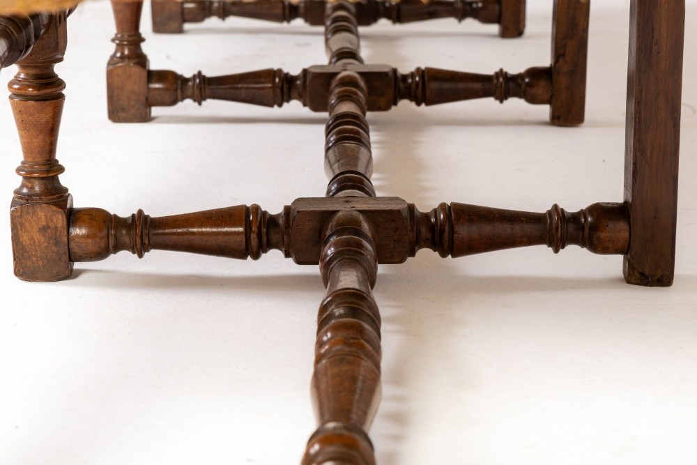 An 18th-century Italian walnut settee featuring high-backed wings, flame-stitch patterned upholstery in warm ochre tones, and six turned wood legs connected by stretchers. View IX