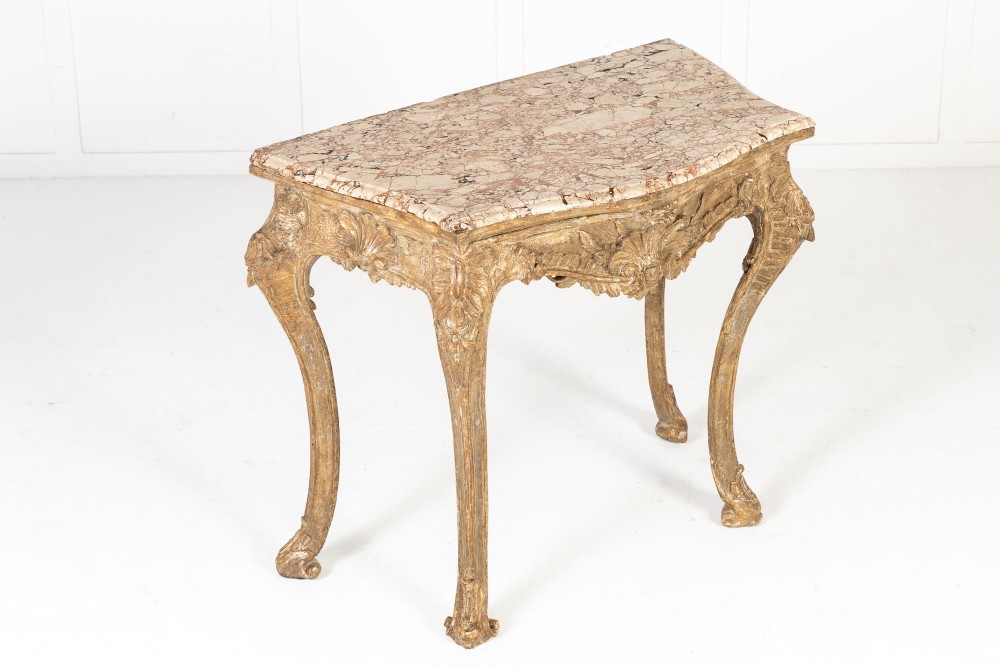 An 18th-century Italian Rococo silver-gilt console table featuring carved leaf motifs, cabriole legs, and a rectangular pink marble top.