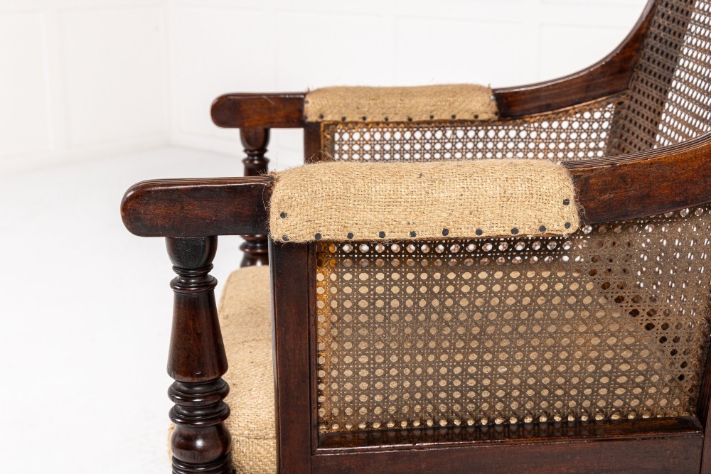 A Regency dark mahogany bergere library armchair featuring woven cane back and side panels, turned front legs on brass castors, and upholstered armrests. View II