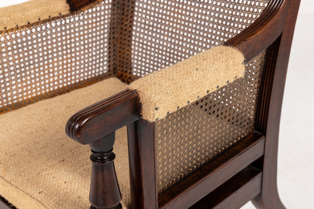 A Regency dark mahogany bergere library armchair featuring woven cane back and side panels, turned front legs on brass castors, and upholstered armrests. View III