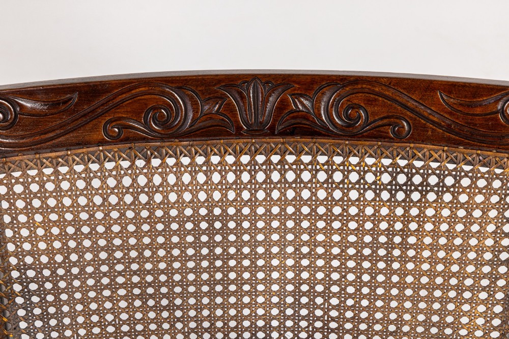 A Regency dark mahogany bergere library armchair featuring woven cane back and side panels, turned front legs on brass castors, and upholstered armrests. View IV