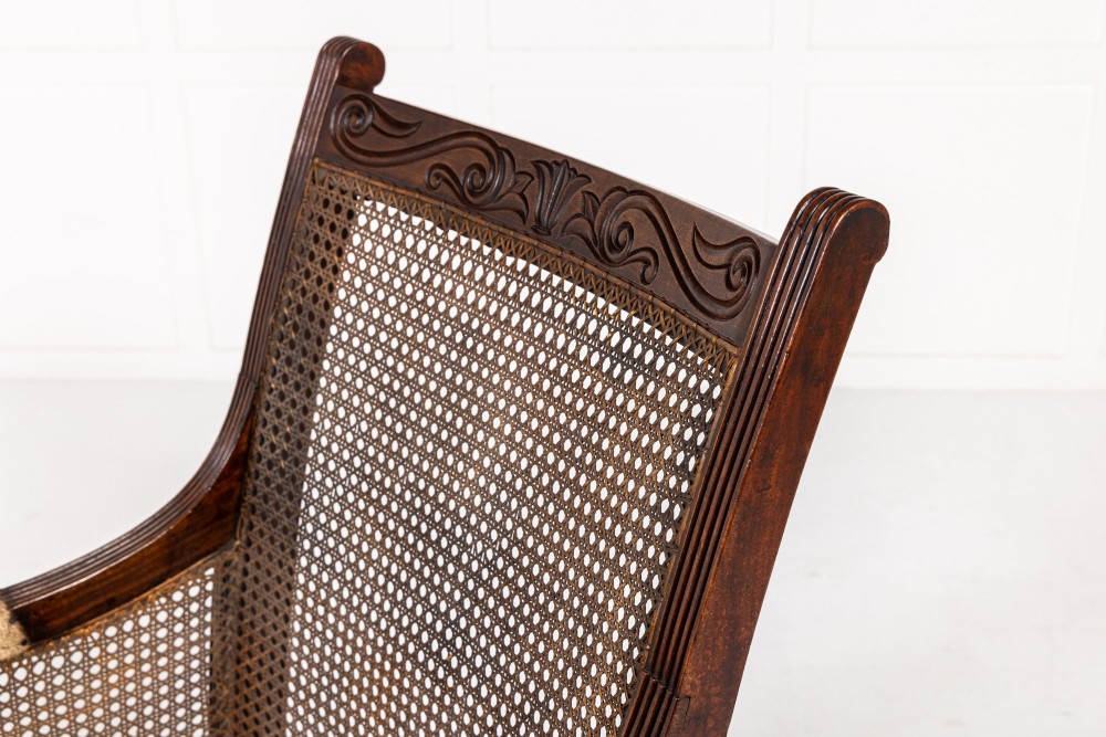 A Regency dark mahogany bergere library armchair featuring woven cane back and side panels, turned front legs on brass castors, and upholstered armrests. View V