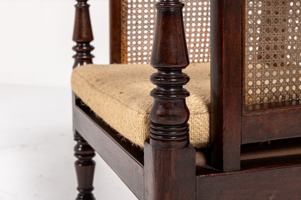 A Regency dark mahogany bergere library armchair featuring woven cane back and side panels, turned front legs on brass castors, and upholstered armrests. View VI