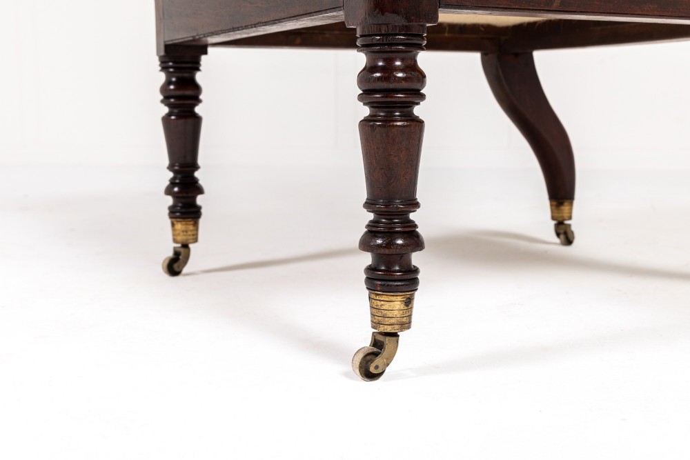 A Regency dark mahogany bergere library armchair featuring woven cane back and side panels, turned front legs on brass castors, and upholstered armrests. View VII