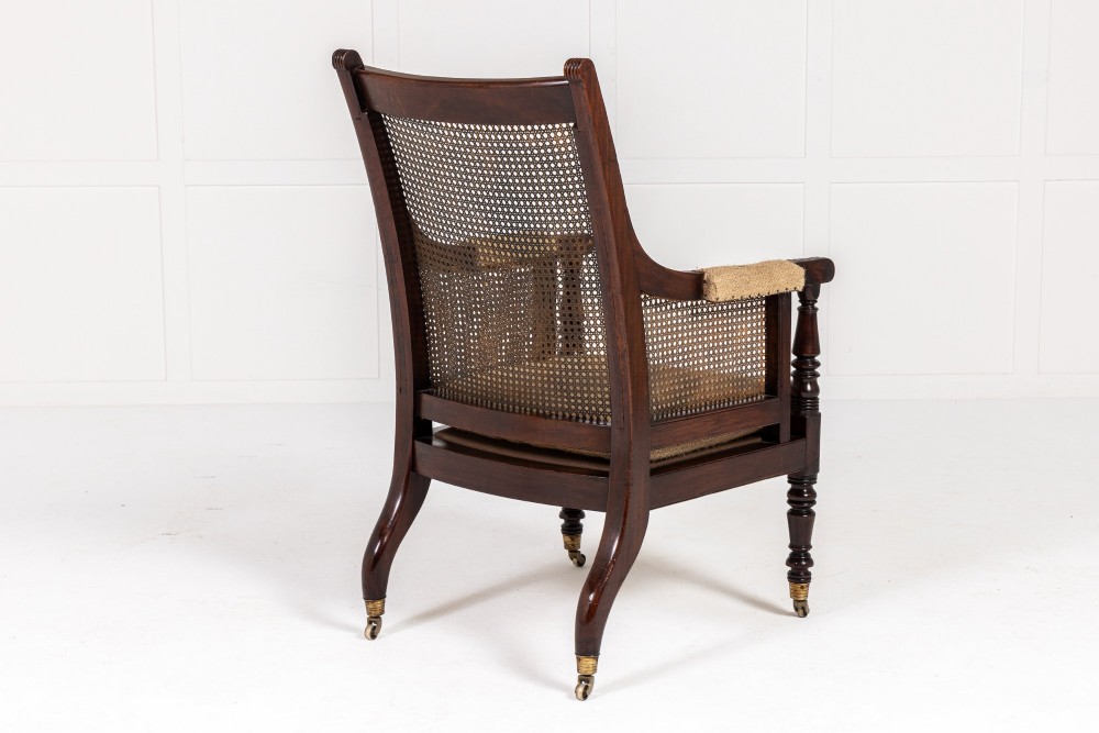 A Regency dark mahogany bergere library armchair featuring woven cane back and side panels, turned front legs on brass castors, and upholstered armrests. View VIII