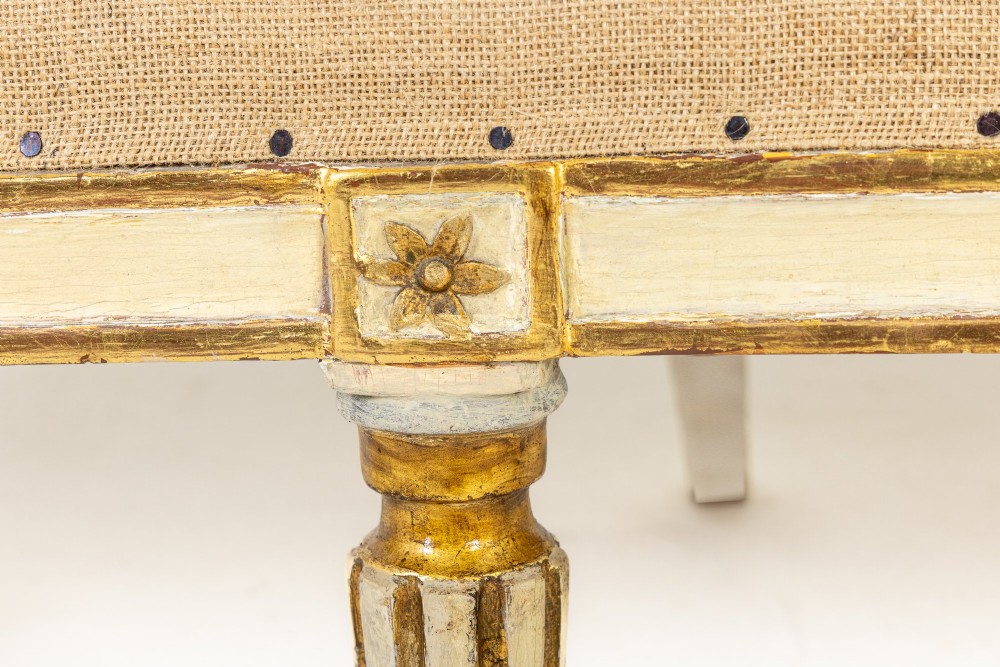 An 18th-century Italian Neoclassical settee featuring a cream-painted frame with gold leaf accents, a curved vertical spindle back, fluted turned legs, and a neutral upholstered seat. View X