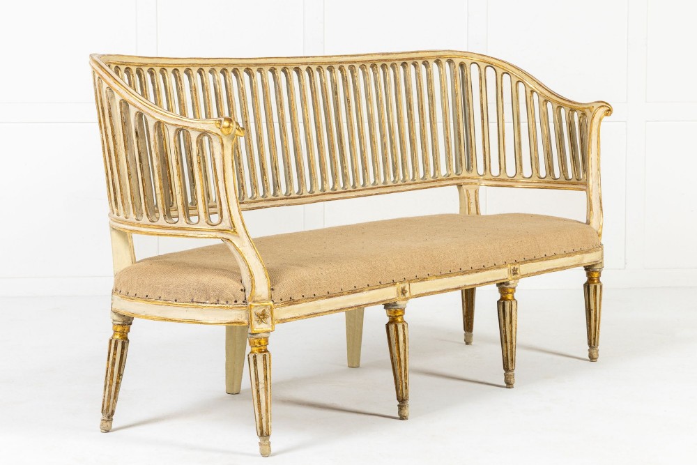 An 18th-century Italian Neoclassical settee featuring a cream-painted frame with gold leaf accents, a curved vertical spindle back, fluted turned legs, and a neutral upholstered seat. View XI