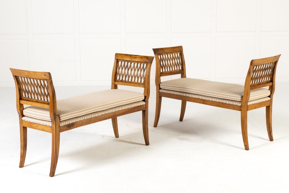 A pair of 19th-century French walnut window seats with carved lattice ends and striped upholstered cushions.