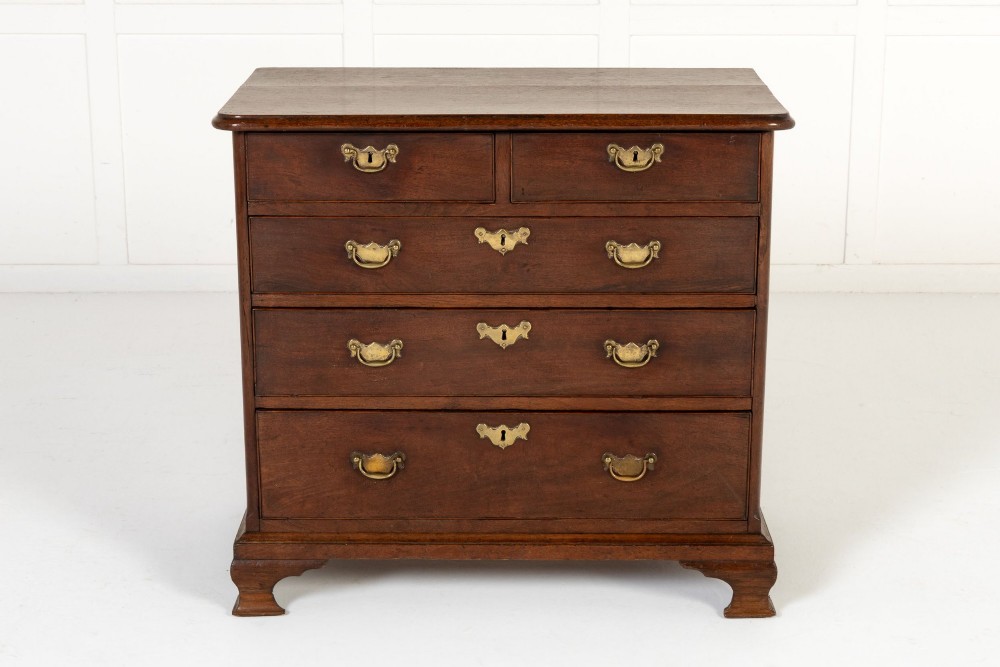 An 18th-century English walnut chest of drawers featuring two short drawers over three long drawers with brass hardware and bracket feet.