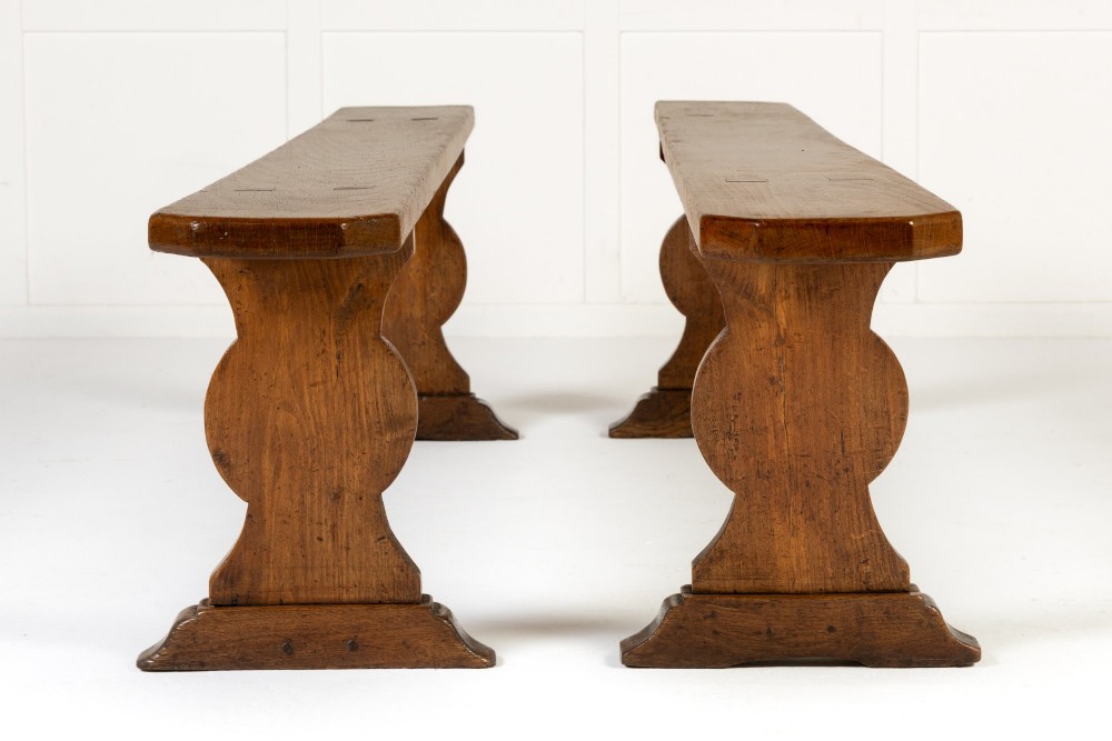 A pair of 19th-century French backless wooden hall benches featuring shaped trestle supports and visible joinery. View III