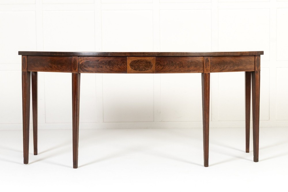 An 18th-century Georgian mahogany serving table featuring a curved apron with central oval inlay and four tapered square legs.