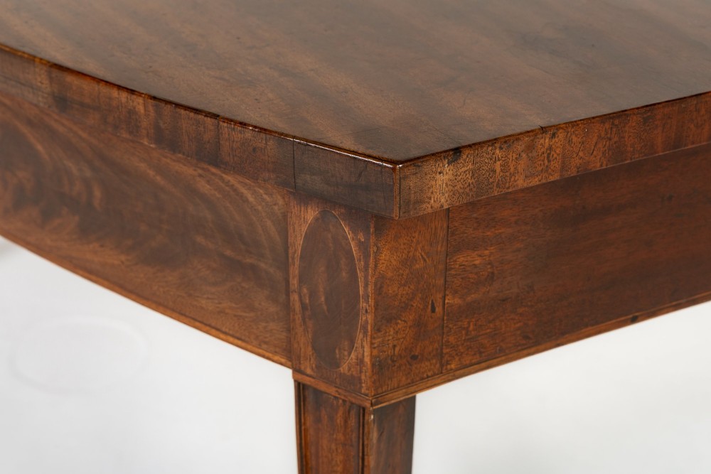An 18th-century Georgian mahogany serving table featuring a curved apron with central oval inlay and four tapered square legs. View VI