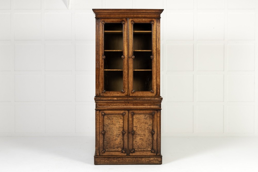 A tall 19th-century English pollard oak bookcase featuring a glazed two-door upper section and a solid panelled lower cupboard with circular boss details.