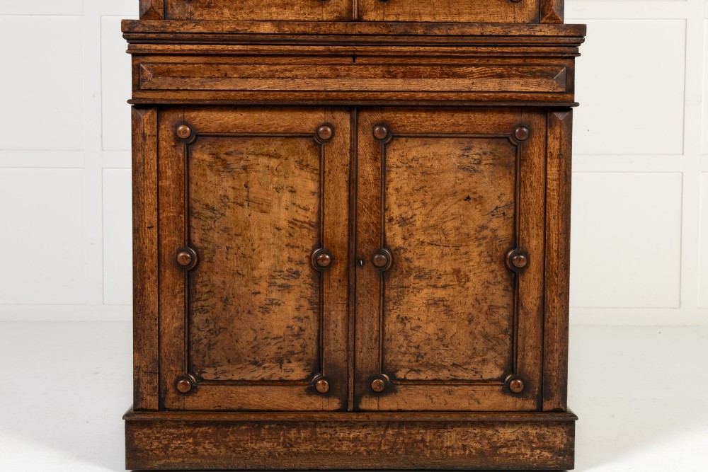 A tall 19th-century English pollard oak bookcase featuring a glazed two-door upper section and a solid panelled lower cupboard with circular boss details. View VI