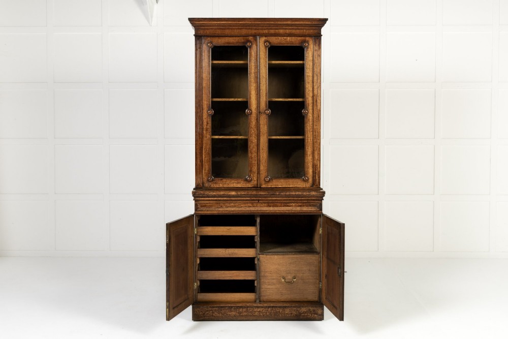 A tall 19th-century English pollard oak bookcase featuring a glazed two-door upper section and a solid panelled lower cupboard with circular boss details. View VII