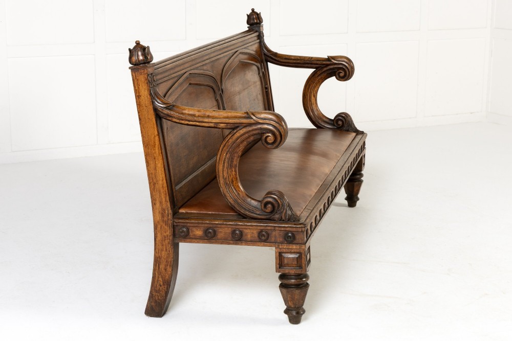 A nineteenth-century carved dark oak Gothic Revival bench featuring pointed arches on the backrest, scrolled armrests, and a fitted leather seat. View II