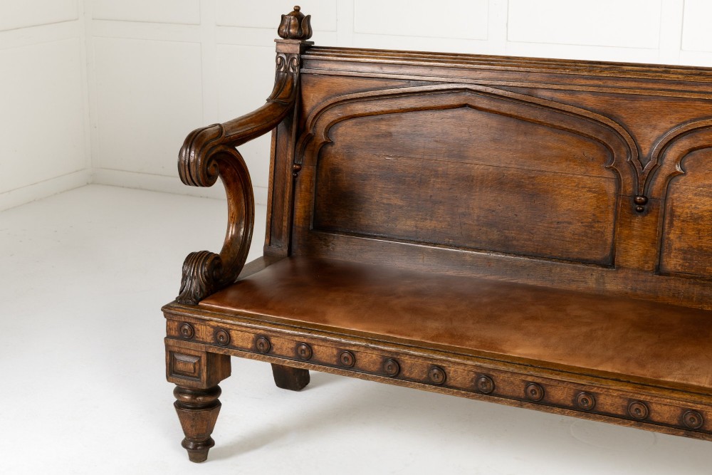 A nineteenth-century carved dark oak Gothic Revival bench featuring pointed arches on the backrest, scrolled armrests, and a fitted leather seat. View III