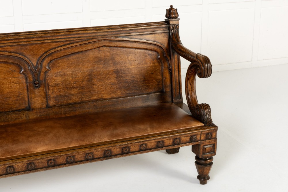 A nineteenth-century carved dark oak Gothic Revival bench featuring pointed arches on the backrest, scrolled armrests, and a fitted leather seat. View IV