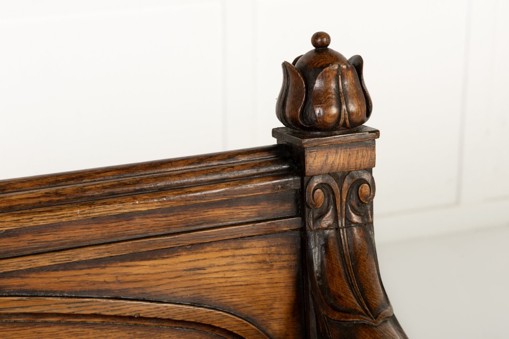 A nineteenth-century carved dark oak Gothic Revival bench featuring pointed arches on the backrest, scrolled armrests, and a fitted leather seat. View V