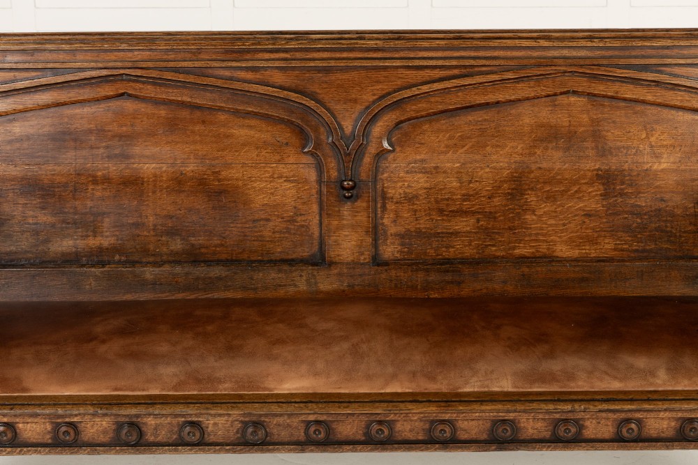 A nineteenth-century carved dark oak Gothic Revival bench featuring pointed arches on the backrest, scrolled armrests, and a fitted leather seat. View IX