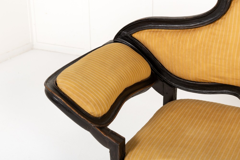 An 18th-century Italian ebonised sofa featuring a high serpentine backrest, mustard yellow striped upholstery, and carved cabriole legs. View II
