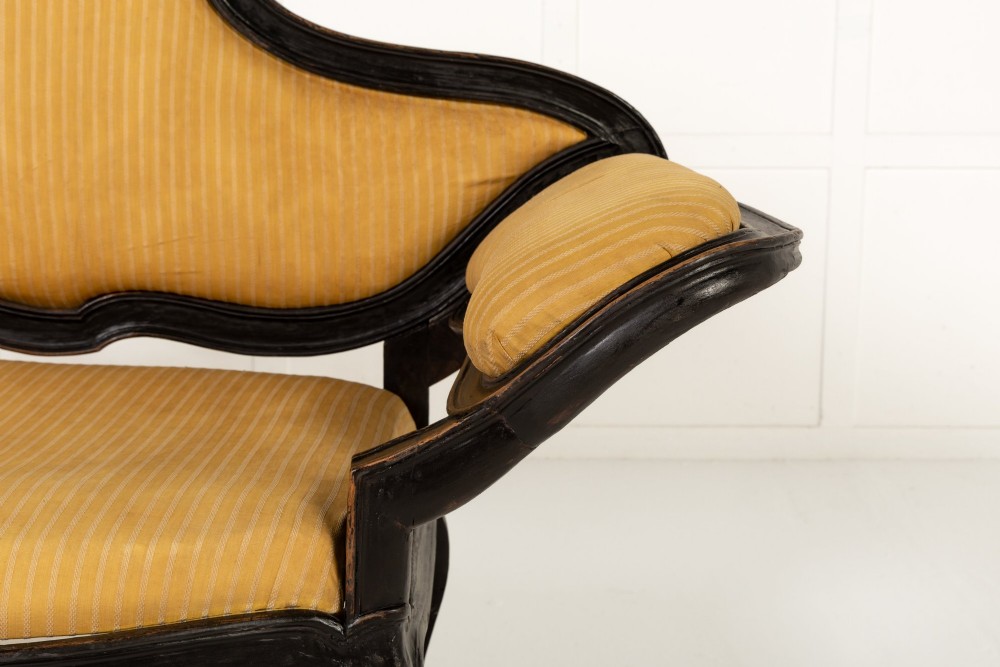 An 18th-century Italian ebonised sofa featuring a high serpentine backrest, mustard yellow striped upholstery, and carved cabriole legs. View III